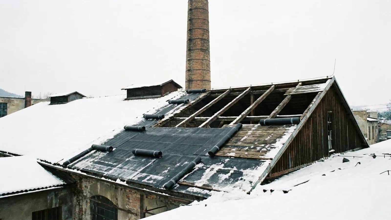 Sedlová střecha průmyslové kotelny s rozdělanou hydroizolací a komínem v zimě.