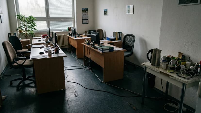 Prázdná kancelář s prodlužovacím kabelem přes cestu a rychlovarnou konvicí na přeplněném stolku.